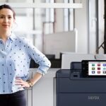 Una donna in piedi accanto alla stampante Xerox® PrimeLink® Serie C9200 in un ufficio moderno